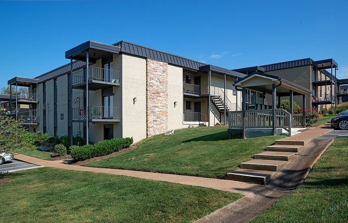 Scenic view of a charming apartment building with balconies and well-manicured green lawns under a blue sky.