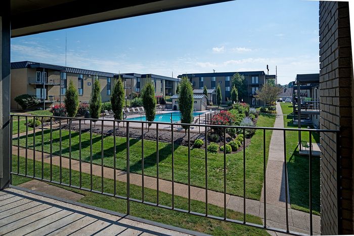 Balcony view of a charming apartment complex with a central swimming pool and lush landscaping.