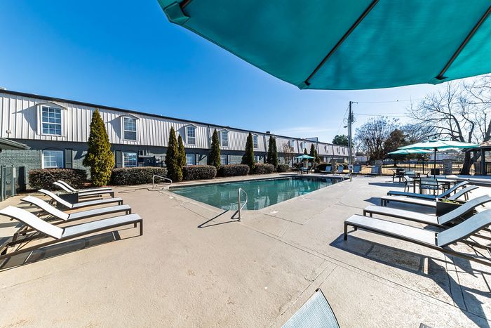 Inviting outdoor swimming pool area with sun loungers and vibrant umbrellas under a clear blue sky.
