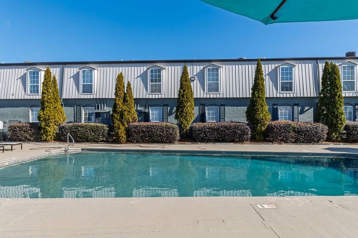 Inviting apartment pool with clear blue water, surrounded by landscaped gardens and modern building architecture.