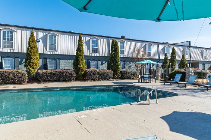 Elegant apartment complex featuring a sparkling outdoor pool with lounge chairs and umbrellas.
