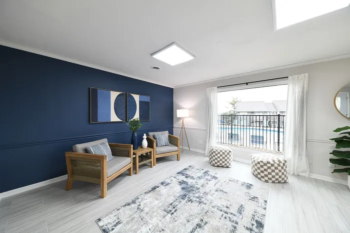 Bright living room with stylish decor, featuring a navy accent wall, modern seating, and large window overlooking a pool.