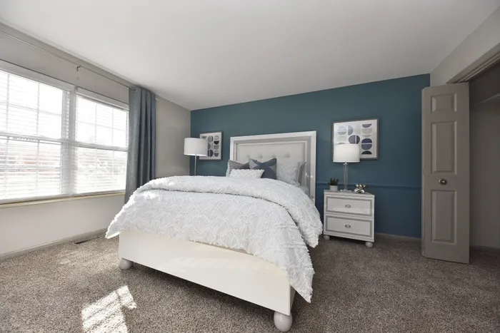 Elegant bedroom featuring calming blue accent wall, plush white bedding, and natural light from large windows.