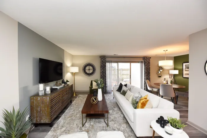 Elegant living room with a modern sofa, stylish decor, and a dining area with natural lighting.