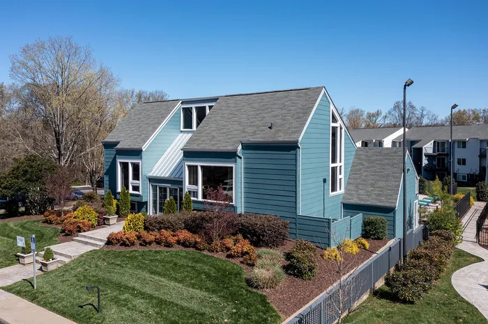 Charming blue apartment building with modern architecture, surrounded by lush landscaping and vibrant greenery on a sunny day.
