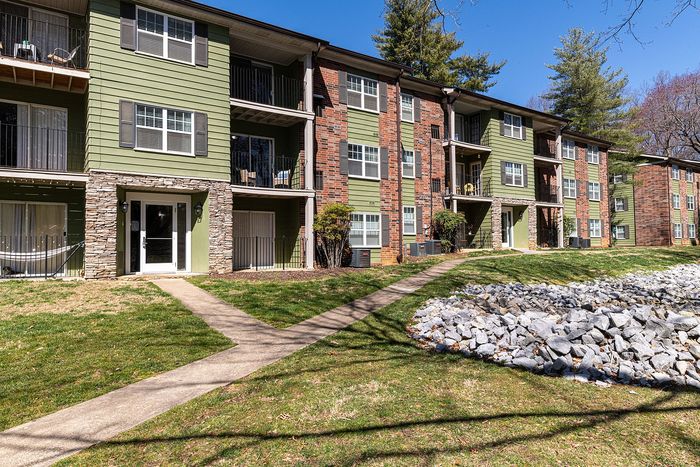 Charming apartment complex with modern green and brick exterior, featuring private balconies and lush landscaped surroundings.