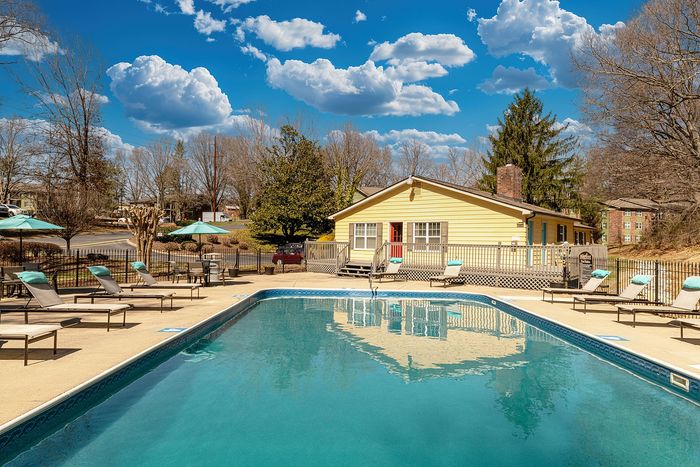 Inviting outdoor pool area with sun loungers and umbrellas, set against a charming yellow house and vibrant blue sky.