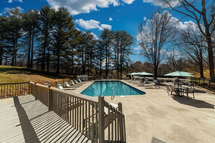 Serene outdoor pool area with loungers and umbrellas, surrounded by lush trees and blue skies, perfect for relaxing getaways.
