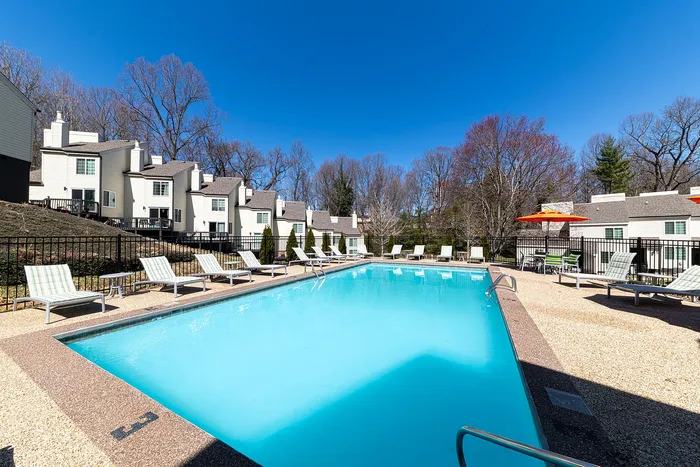 Inviting outdoor swimming pool surrounded by modern townhouses, featuring comfortable lounge chairs and vibrant umbrellas under a clear blue sky.