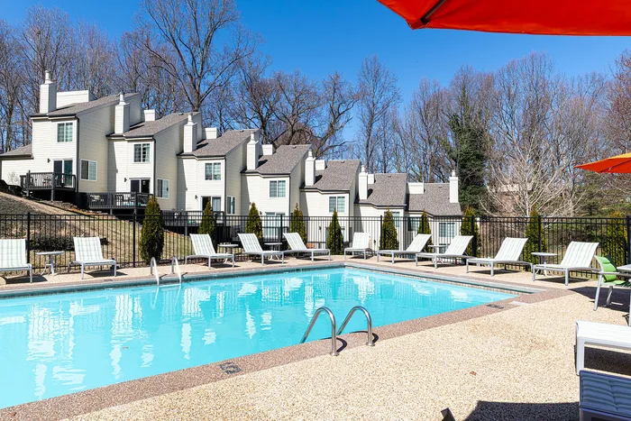 Inviting apartment complex with modern townhouses and a sparkling outdoor pool surrounded by stylish lounge chairs, perfect for relaxation and enjoyment.