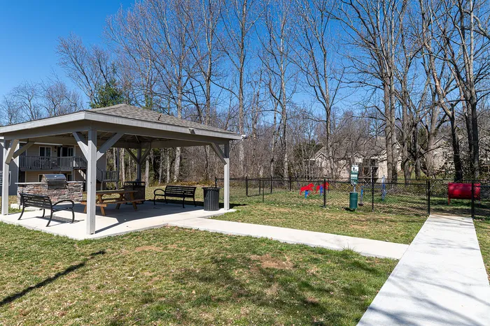 Charming outdoor pavilion with seating and grill area, surrounded by lush green space and a playground, perfect for gatherings and relaxation.