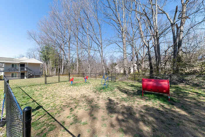 Spacious fenced play area with vibrant children's equipment, surrounded by serene trees and a charming residential building.