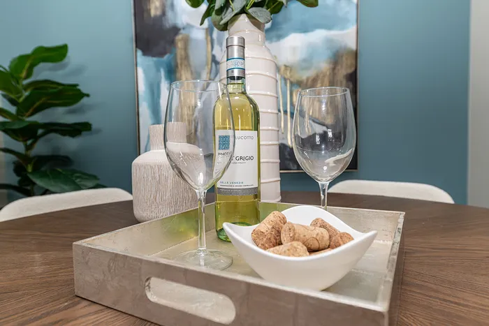 Elegant dining setup with a bottle of Pinot Grigio, wine glasses, and corks on a chic tray, surrounded by stylish decor and greenery.