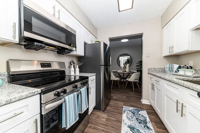 Contemporary kitchen with sleek stainless steel appliances, white cabinetry, and granite countertops leading to a cozy dining area.