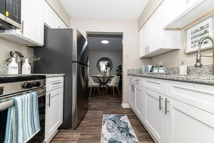 Modern kitchen with sleek white cabinets, granite countertops, and stainless steel appliances, leading into an elegant dining area with a stylish table and chairs.