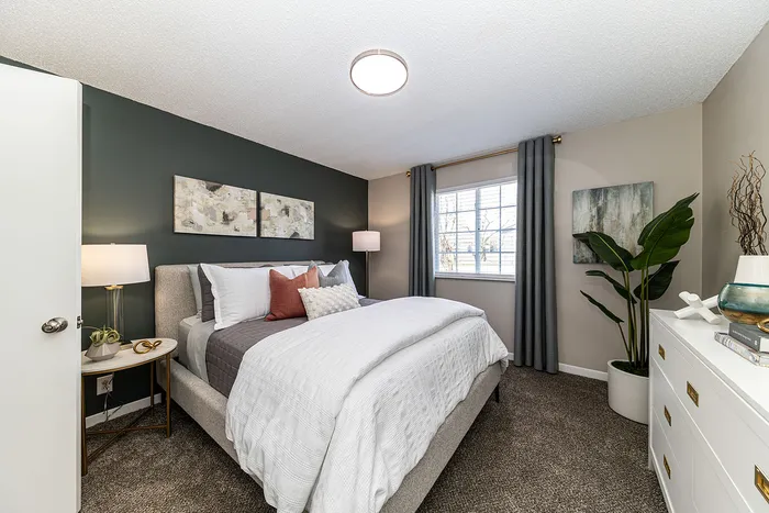 Elegant bedroom with modern gray tones, featuring a cozy bed, stylish decor, and natural light through a large window.