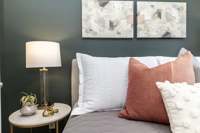 Elegant bedroom corner featuring a cozy bed with white and terracotta pillows, modern art pieces, and a stylish side table lamp.