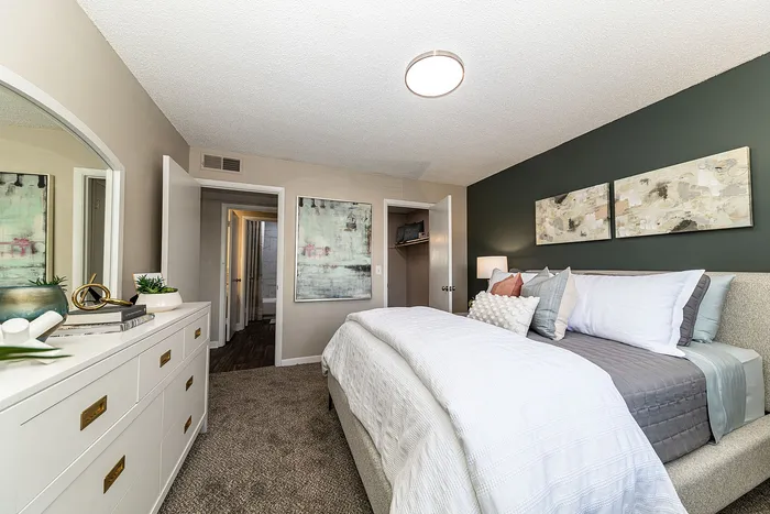 Elegant bedroom showcasing a plush bed with stylish pillows, modern artwork, and a sleek white dresser for a cozy retreat.