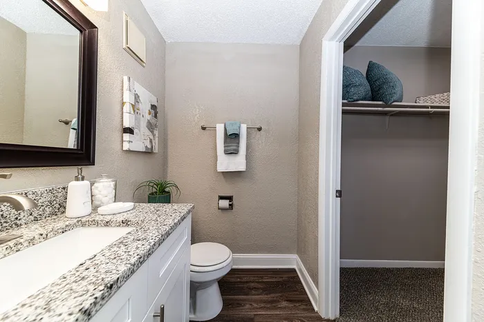Modern bathroom with sleek granite countertop, elegant white vanity, and spacious open closet.
