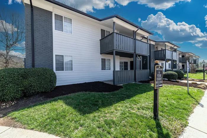 Charming two-story apartment complex with private balconies, lush landscaping, and wheelchair access under a vibrant blue sky.