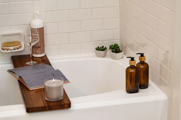 Luxurious bathroom retreat with a elegant bathtub setup, wooden bath board featuring a candle, book, wine glass, and chic decor, perfect for relaxation.
