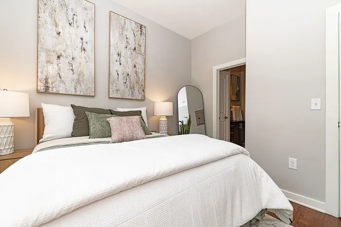 Elegant bedroom with plush bedding, modern artwork, and a stylish full-length mirror, offering a serene retreat.