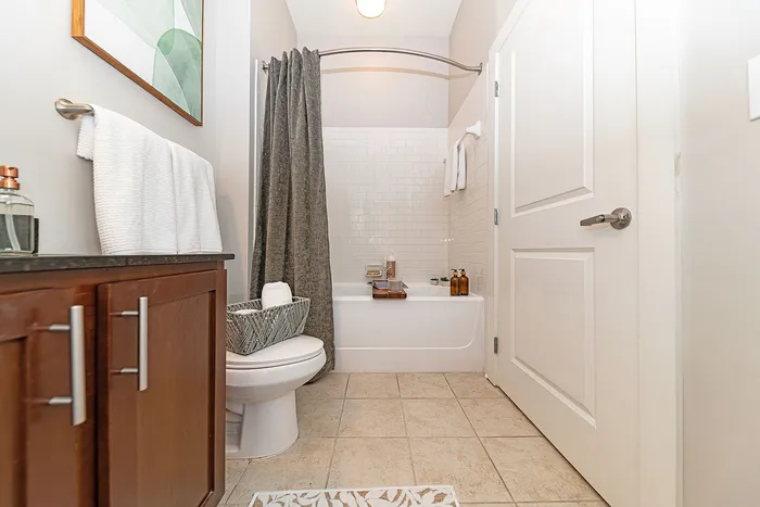 Elegant bathroom with modern fixtures, featuring a pristine bathtub with trendy tiled walls, sleek wooden cabinetry, and tasteful decor.