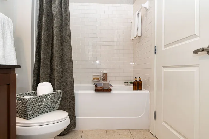 Chic bathroom with modern design, featuring a white subway tile tub, stylish gray shower curtain, and elegant countertop accents.