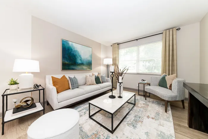 Bright and inviting living room with a chic white sofa, stylish cushions, and a modern coffee table. Large window brings in natural light over an elegant rug and contemporary decor.