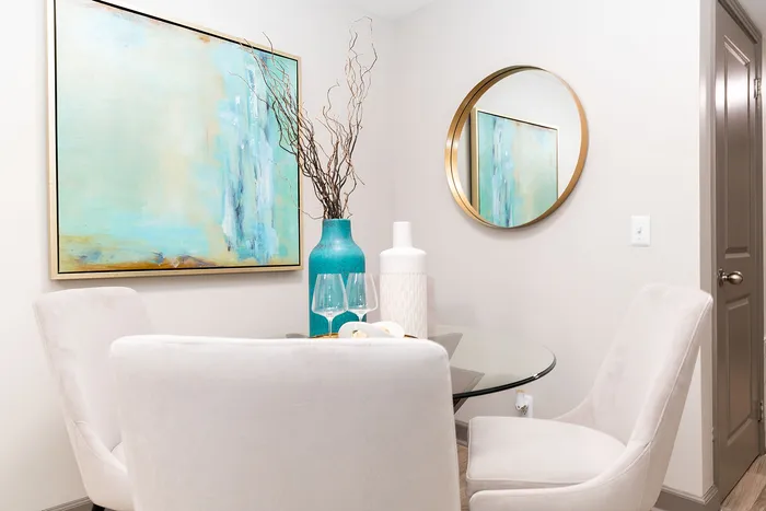 Elegant dining nook with plush white chairs, a glass table, and a vibrant teal abstract painting creating a serene ambiance.