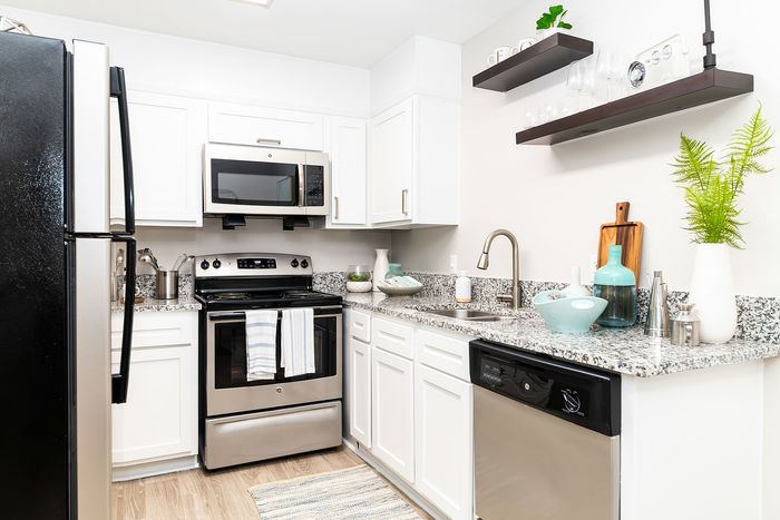 Modern kitchen with sleek stainless steel appliances, granite countertops, and elegant white cabinetry, accentuated by vibrant decor and open shelving.