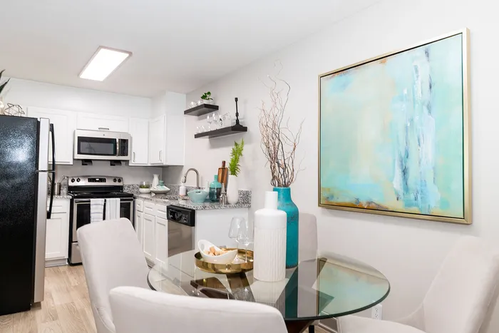 Modern kitchen and dining area with sleek white cabinetry, granite countertops, and vibrant decor featuring teal accents and a large abstract painting.
