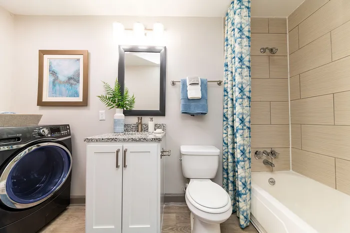 Modern bathroom with elegant granite countertop, stylish mirror, and vibrant decor including a washing machine and blue patterned shower curtain.
