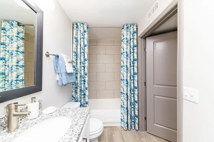 Bright and modern bathroom with elegant granite countertop, stylish fixtures, and vibrant blue patterned shower curtains.