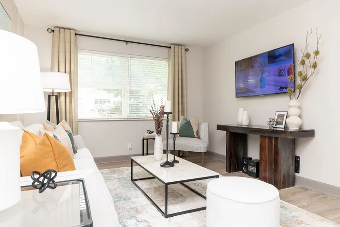 Bright and stylish living room with modern decor, featuring cozy seating, a large window, and a wall-mounted TV.