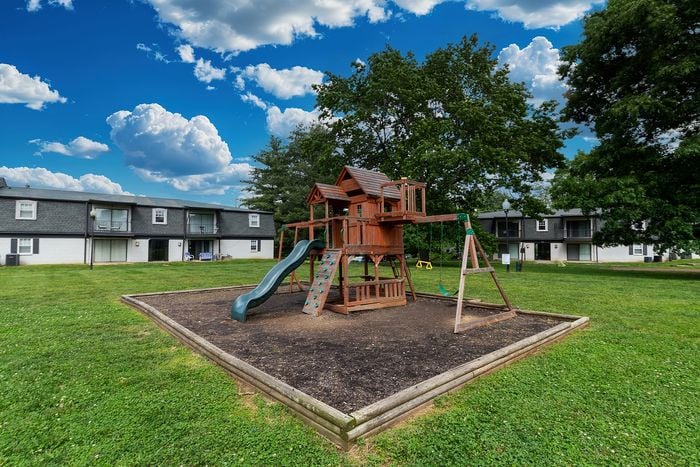 Inviting apartment complex with charming playground and lush green surroundings under a vibrant blue sky.