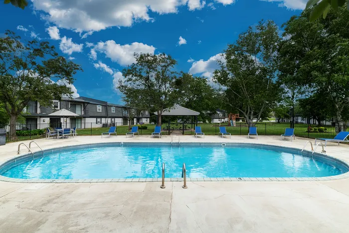 Inviting outdoor pool area surrounded by lush greenery, featuring cozy lounge chairs and a charming gazebo, perfect for relaxation.