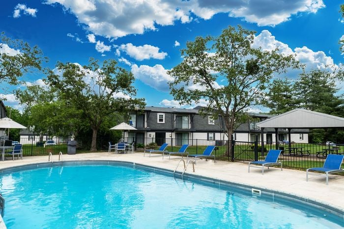 Inviting apartment community featuring a sparkling outdoor pool, surrounded by lush greenery and modern poolside seating under a blue sky.