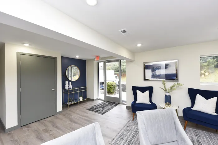 Modern living area with elegant decor, featuring plush blue armchairs, stylish rugs, and a chic console table with artistic accents.