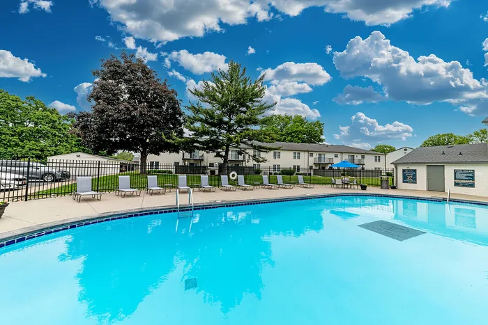 Inviting outdoor pool area with pristine blue water, surrounded by sun loungers and lush greenery under a vibrant blue sky.