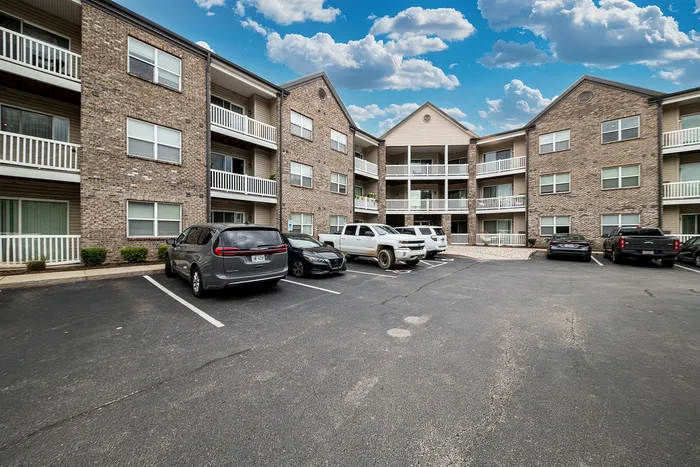 Charming three-story apartment complex with brick facade and spacious balconies, showcasing convenient parking and a welcoming atmosphere under a bright blue sky.