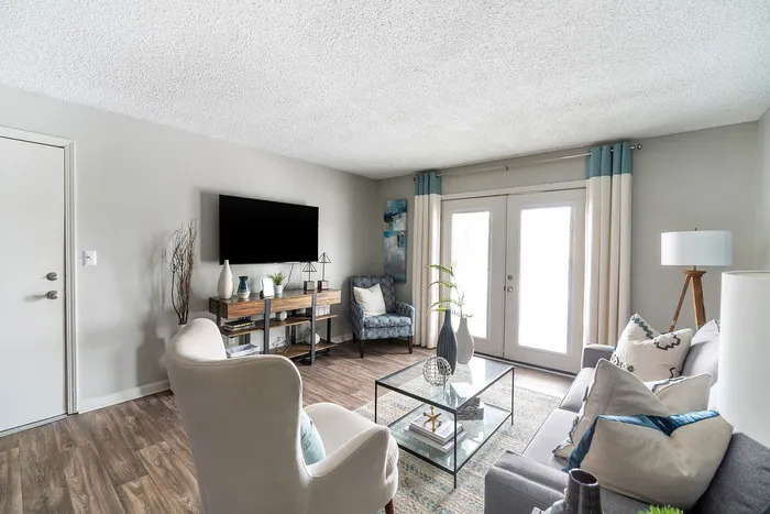 Chic and modern living room featuring elegant decor, a cozy grey sofa, glass coffee table, and bright natural light from French doors.