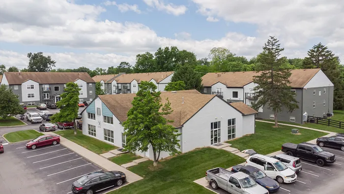 Inviting apartment community with modern design, ample parking, and lush green surroundings on a sunny day.