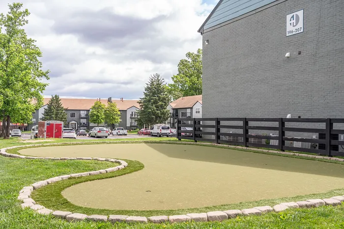 Charming apartment community featuring a mini putting green, surrounded by lush greenery and modern buildings, perfect for leisure and relaxation.