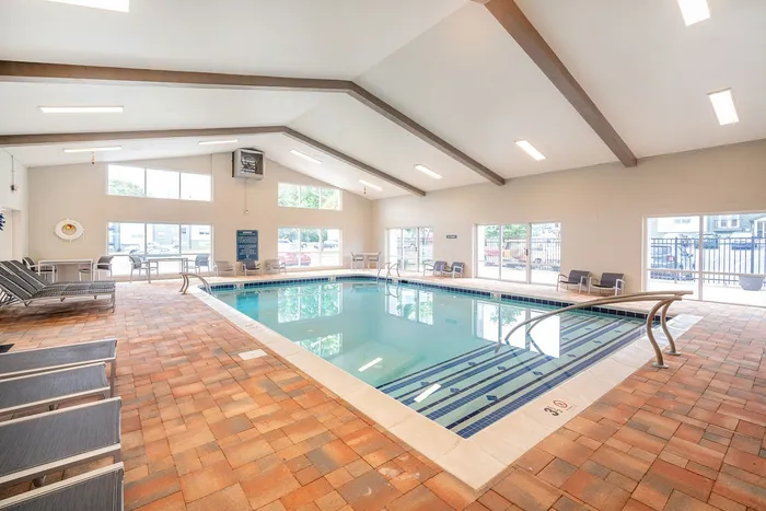 Bright and inviting indoor swimming pool with modern lounge chairs and large windows, perfect for relaxation and leisure.