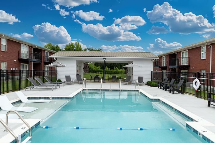 Charming outdoor pool area with sun loungers and umbrellas, surrounded by modern brick apartment buildings under a vibrant sky.