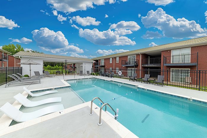 Inviting community pool area with modern lounge chairs, surrounded by brick buildings and a vibrant blue sky.