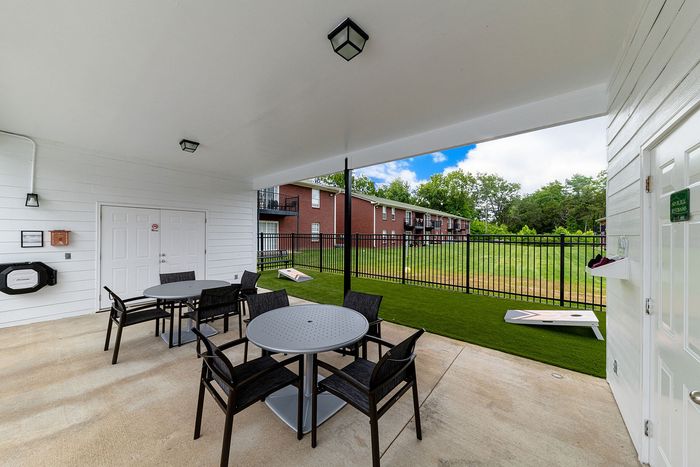 Charming outdoor seating area with modern round tables, overlooking a lush green lawn and a red-brick apartment building backdrop.