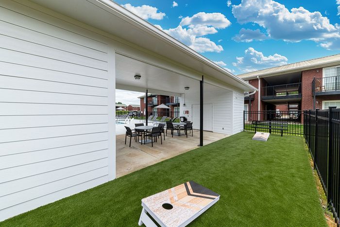 Charming outdoor community area with covered patio, seating, and playful cornhole space, perfect for relaxing and socializing.