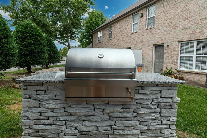 Elegant outdoor grill on a stylish stone countertop, surrounded by lush greenery and modern brick architecture.